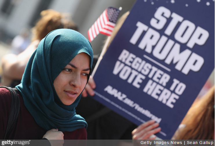 Muslim woman in front of an anti-Trump sign