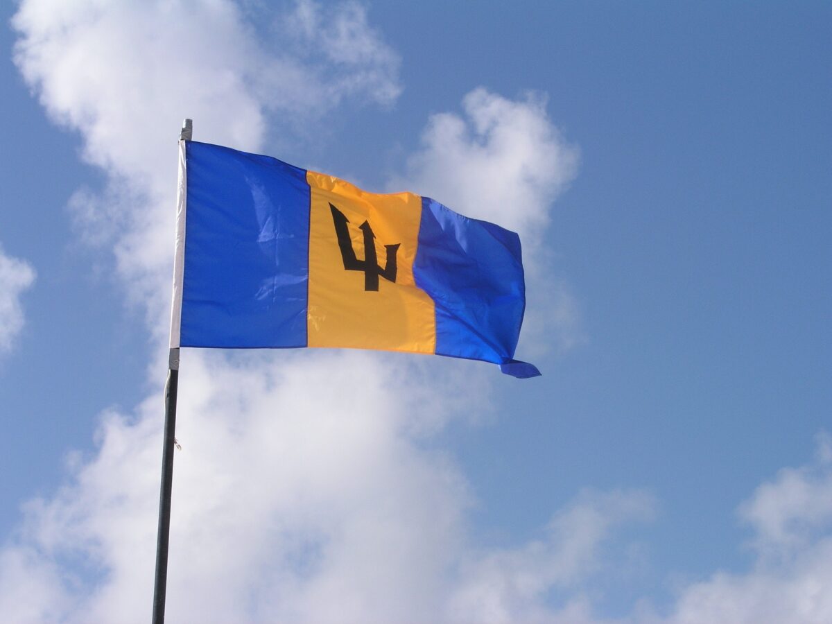 Flag of Barbados with a blue sky background and scattered white clouds